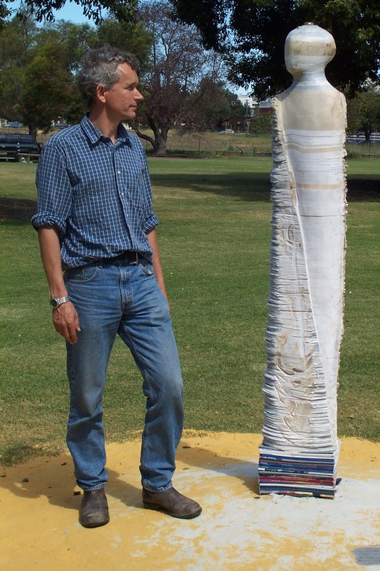 Photo of Artist Graham Hay with sculpture called Bureaucrat I, which was made in 2002.  This is an outside sculpture made from Government documents.  It measures 200 x 40 x 20 cm.  Photo by Frances Dennis.